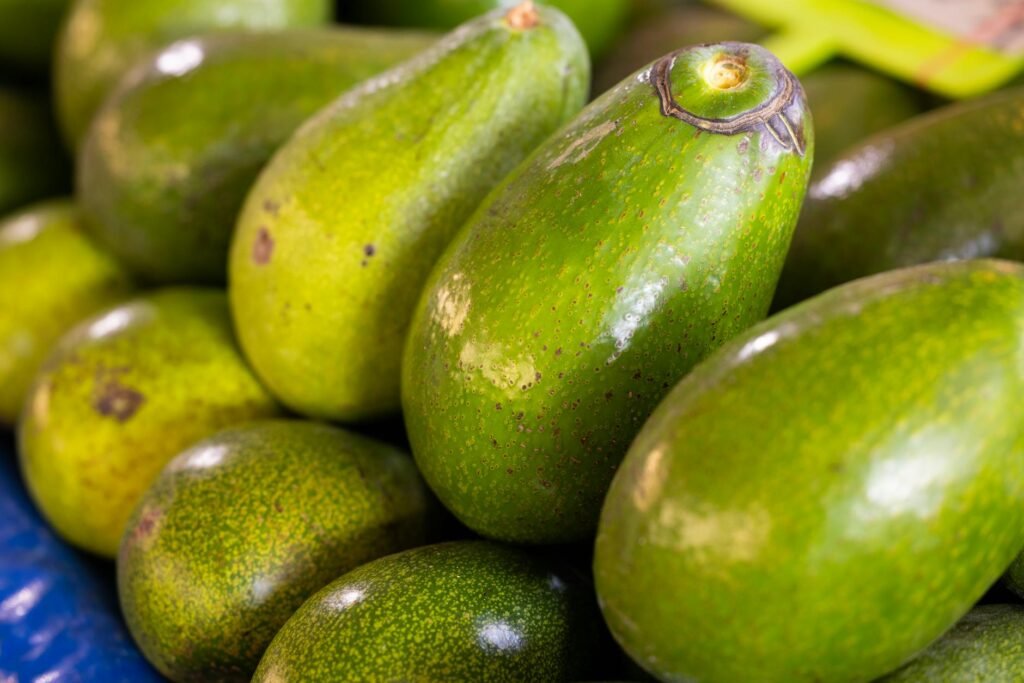Several avocados at different ripeness stages arranged on a kitchen counter next to a paper bag