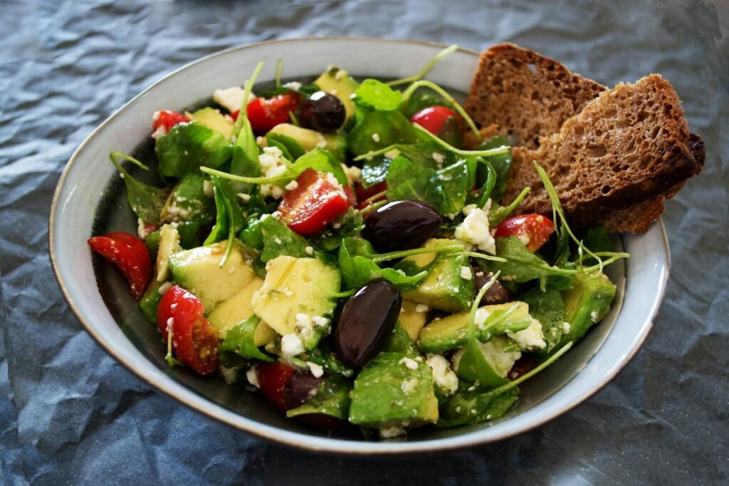 A chicken and avocado lunch bowl with tomatoes, cucumber, and greens
