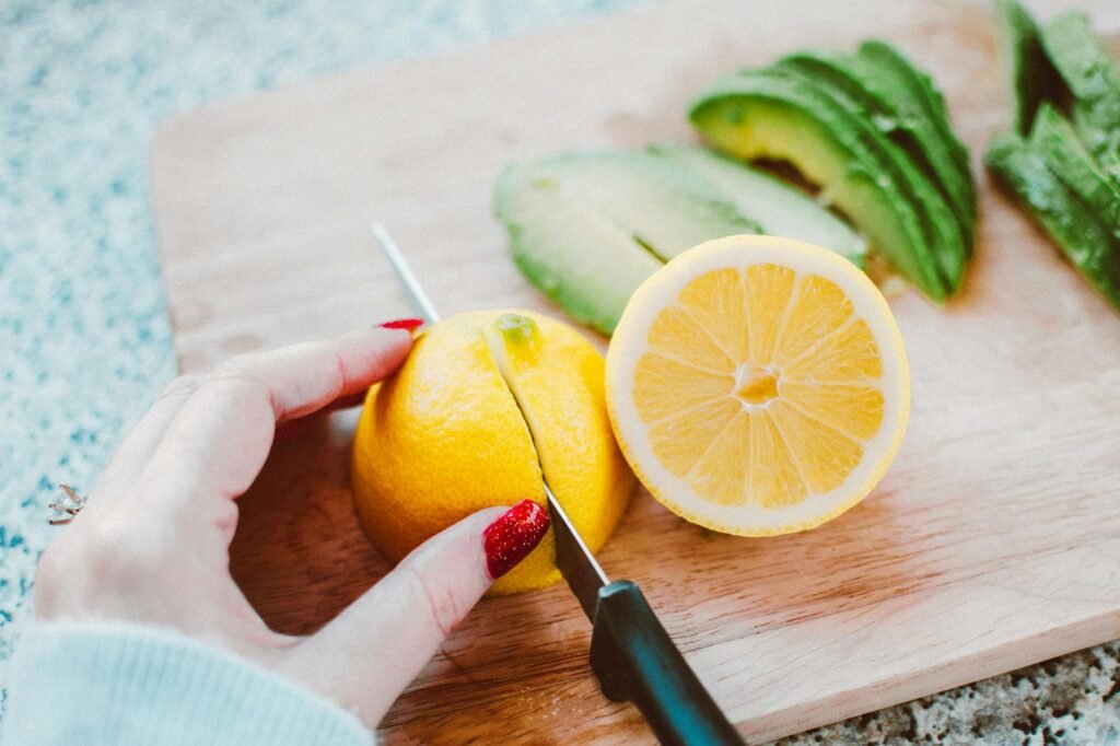 A cut avocado beside lemon halves, wrap, and a storage container on a clean counter.