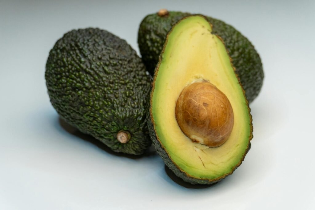 A halved avocado with light surface browning on a kitchen board next to a spoon and lemon