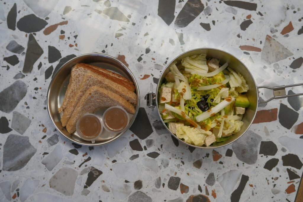 Separate containers of greens, vegetables, dressing, and avocado for a packed lunch salad