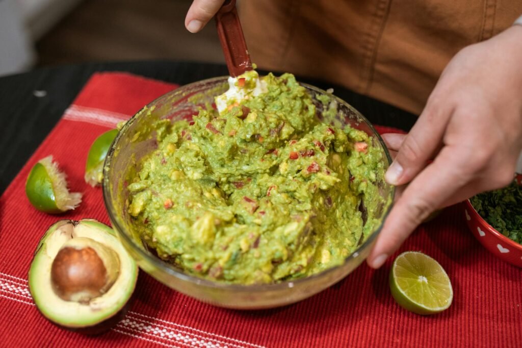 Hands mashing white beans and avocado in a bowl with lemon nearby
