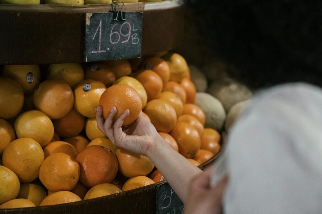 A shopper's hand checking avocados in a grocery store produce display