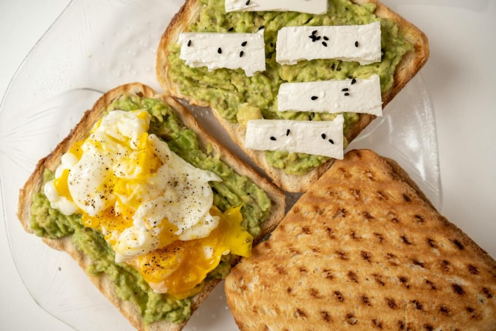 Ingredients for avocado toast arranged with eggs, tomato, whole-grain bread, and a measured portion of avocado.
